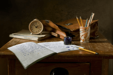 Table de chever avec un carnet, un vieux sac, un réveil et de quoi écrire